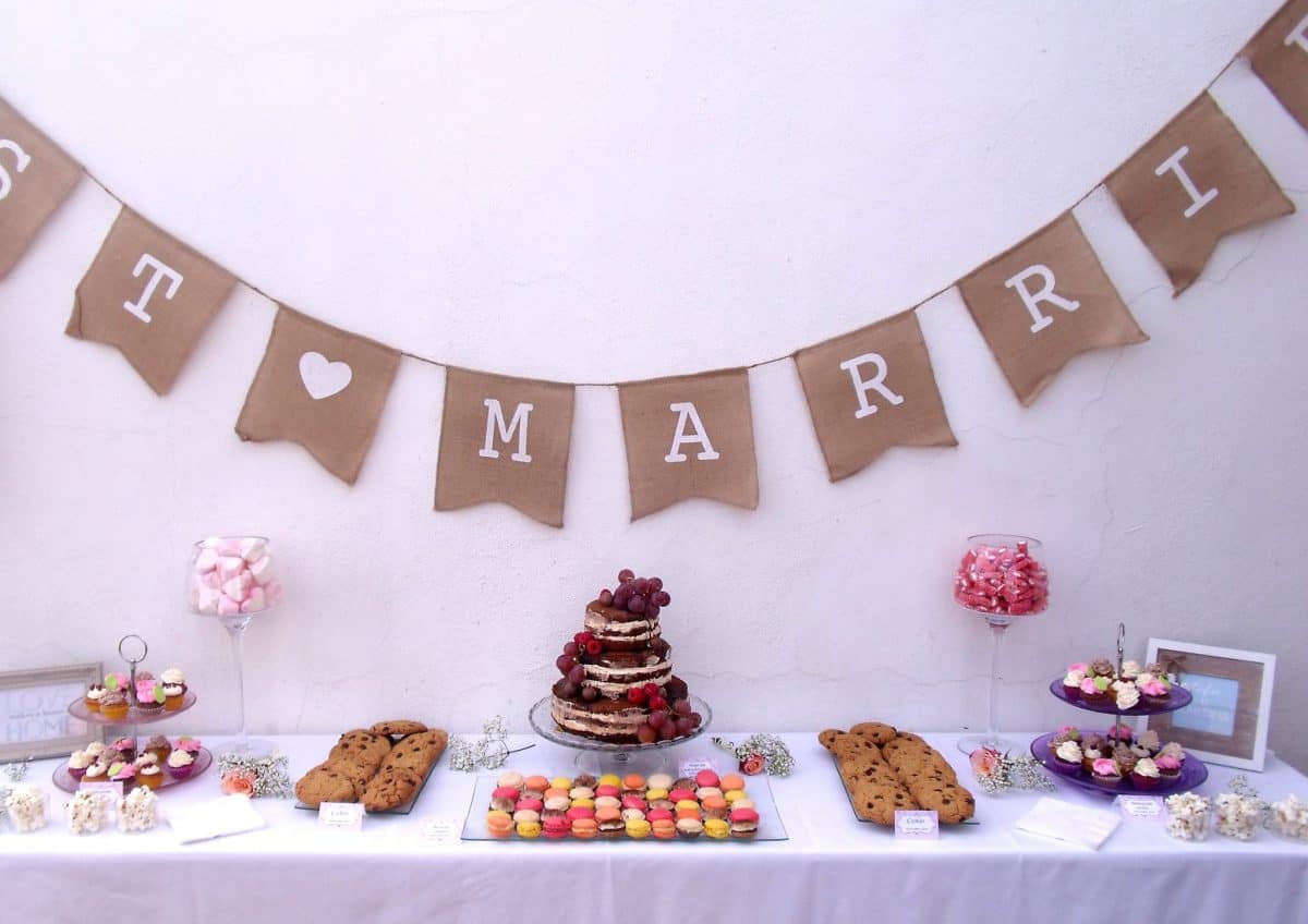 Mesa dulce con tarta desnuda decorada con frutos rojos, gominolas, mini Cupcakes, macarons y galletas con chispas de chocolate