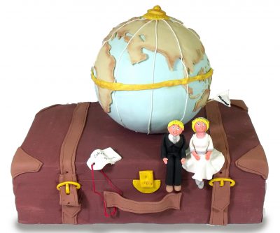 tarta rectangular con forma de maleta, decorada con una bola del mundo y dos figuras de novios sentados encima de la maleta