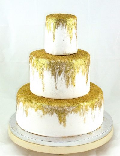 Tarta de tres pisos cubierta de fondant blanco y pintada con un tono dorado.