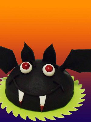 Tarta con forma redondeada cubierta de fondant negro dando forma al cuerpo de un murciélago y unas alas de fondant negro colocadas a cada lado de la tarta.