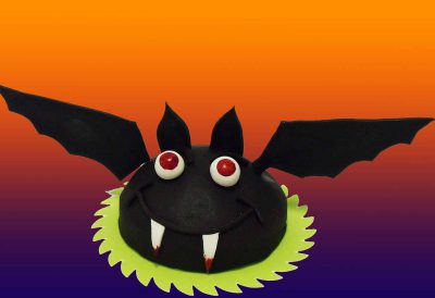 Tarta con forma redondeada cubierta de fondant negro dando forma al cuerpo de un murciélago y unas alas de fondant negro colocadas a cada lado de la tarta.
