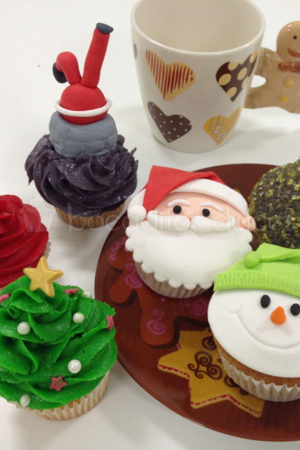 Cupcakes con buttercream de distintos colores, decorados con la cara de papa noel, cara de un muñeco de nieve, papa noel en una pequeña chimenea de fondant y un arbol navideño con buttercream.