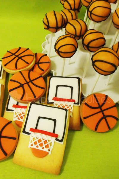 Galletas de mantequilla redondas decoradas con fonant naranja dando forma a un balon de baloncesto, galletas de mantequilla rectangulares decoradas con fondant recreando una canasta de baloncesto.