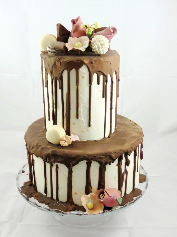 Tarta de dos pisos cubierta de butercream blanco y chocolate negro chorreando y decorada con flores talladas de fondant.