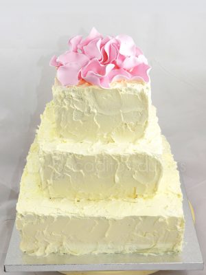 Tarta cuadrada de tres pisos cubierta de buttercream decorada con petalos de rosas modelados en fondant.