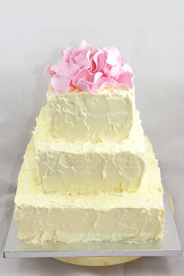 Tarta cuadrada de tres pisos cubierta de buttercream decorada con petalos de rosas modelados en fondant.