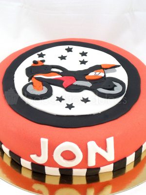 Tarata forrada con fondant rojo, u una cinta de color blanco y negro el nombre de Jon en fondant blanco y una moto modelada en fondanat.