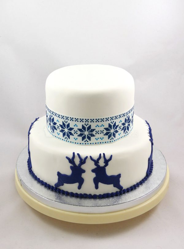 Tarta de dos pisos, cubiertos de fondant blanco, decorada con renos de fondant azul y papel de azucar con motivos nórdicos.