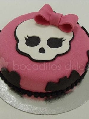 Tarta cubierta de fondant rosas, con murcielagos alrededor en fondant negro y calabera en fondant blanco y lazo tambien de fondante color rosa.