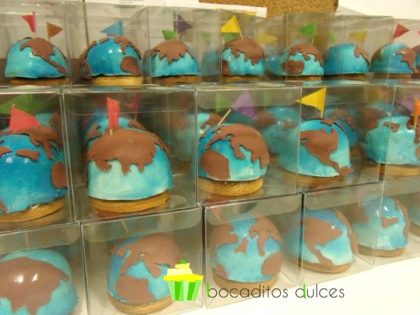 Mini tartar cubiertas de fondant azul decoradas con fondant simulando los continentes en color marron y banderines de colores