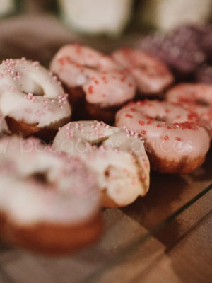 Donuts con glaseado de color blanco decorado con virutitas de caramelo de color rosa, donuts con glaseado de color rosa con virutitas de caramelo de color rojo, donuts con glaseado de color morado con virutitas de color blanco.