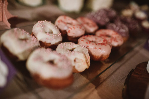Donuts con glaseado de color blanco decorado con virutitas de caramelo de color rosa, donuts con glaseado de color rosa con virutitas de caramelo de color rojo, donuts con glaseado de color morado con virutitas de color blanco.