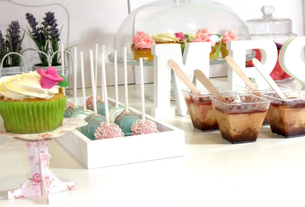 Vasitos de plastico rellenas de diferentes dulces y cake pops decorados con glaseado de color banco, azul y rosa con bolitas blancas.