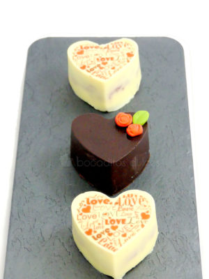 Pequeños pastelitos de frutas, cubiertos con chocolate blanco y con leche, decorados con letras de papel de azúacar, y pequeñas flores de fondant
