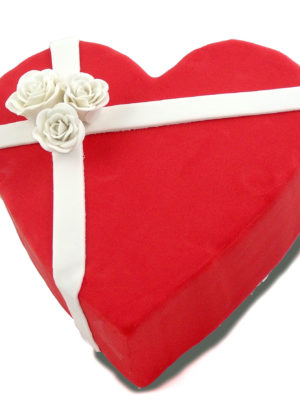Tarta en forma de corazon forrada con fondant de color rojo, y dos tiras de fondant blanco decoradas con tres rosas blancas de fondant