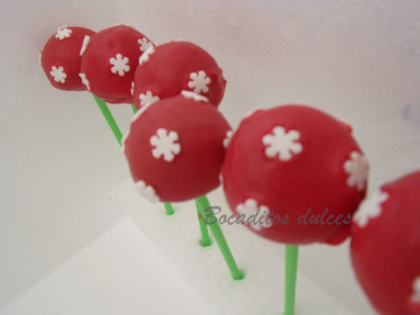 cake pops sencillos navideños con fondo rojo y copos blancos como decoración