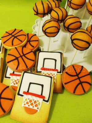 Galletas de mantequilla redondas decoradas con fonant naranja dando forma a un balon de baloncesto, galletas de mantequilla rectangulares decoradas con fondant recreando una canasta de baloncesto.