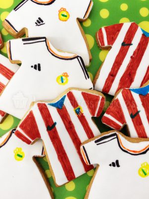 Galletas de mantequilla con forma de camiseta decorada con fondant y la camiseta del Real Madrid cub de Futbol y otra galleta decorada en fondant con la camiseta del Atletico de Madrid.