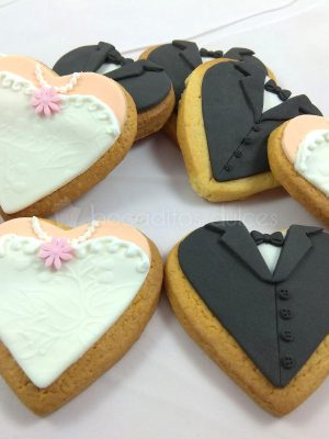 Galletas de mantequilla con forma de corazon decoradas de forma personalizada recreando los trajes de los novios en fondant.
