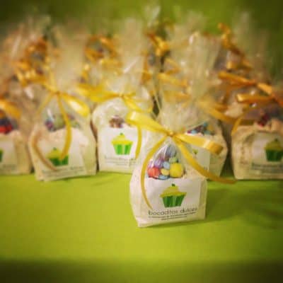 Bolsita de plastico transparente con logotipo personalizado con una variedad de gominolas en su interior cerrada con un lazo color amarillo.