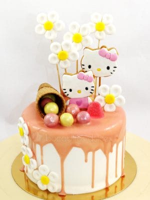 Tarta cubierta de buttercream blanca, con chocolate de fresa chorreando, galletas con la cara de hello kitty, diversas chuches de colores y barquillo de chocolate.