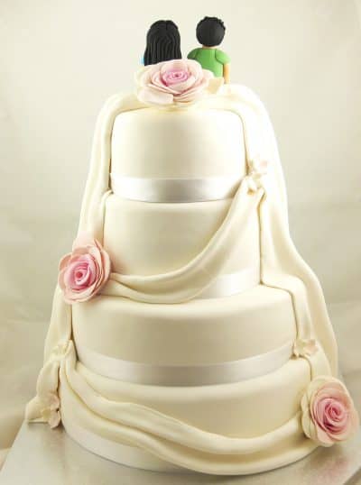 Tarta de cuatro pisos cubierta de fondant blanco cinta de raso alrededor, folres rosas y fondant creando el efecto de tela que cae alrededor.