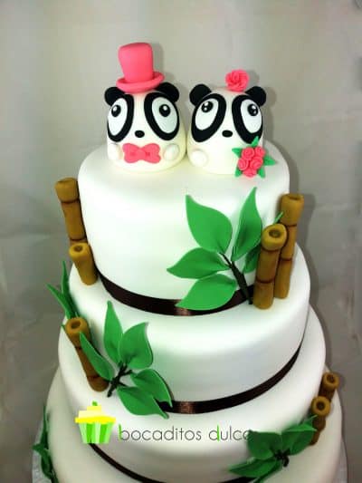 Tarta de cuatro pisos forrados en blanco con una cinta alrededor de raso negro en cada planta decorado con ramas y hojas de fondant y coronada con dos figuritas de osos pandas uno chico vestido de novio y ota de chica.