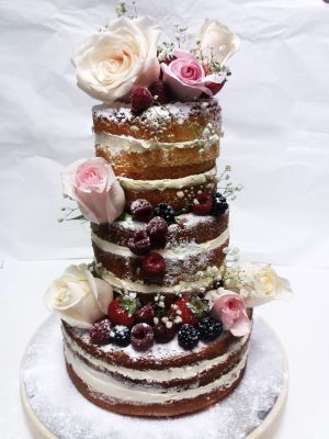 Tarta desnuda de tres pisos decorada con frutos rojos y flores naturales.