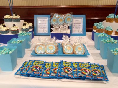 Mesa dulce en color azul, compuesta por cupcakes con buttercream de color azul sabor vailnilla, cajitas de palomitas de color azul, galletas redondas con palo, decoradas con papel comestible de azucar, galletas de mantequilla redondan decoradas con papel comestible de azúcar, bolsitas de chuches, y macarons de color blanco.
