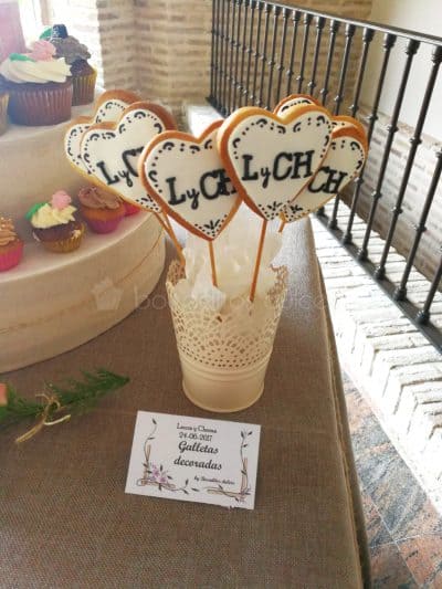 Galletas de mantequilla en forma de corazon con palo, decoradas con fondant blanco y las iniciales de los novios en esta ocasion.