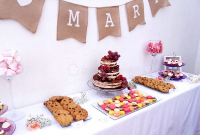 Mesa dulce de estilo rustico compuesta por minicupcakes de distintos sabores, galletas con chips de chocolate, macarons de distintos sabores y tarta de desnuda de tres pisos decorada con frutas del bosque.