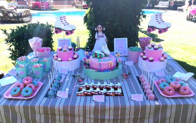 Mesa dulce en colores rosa y verde compuesta por donuts con glaseado en color rosa y verde y decorados con bolitas de caramelos de distintos colores, minicupcakes con buttercread de fresa y chocolate blanco, cakepops cubiertos de candy mels rosa y azul, con bolitas de caramelos de colres,galletas de mantequilla con forma de patin, distintios tipos de gominolas, cajitas de palomitas y para terminar una tarta cubierta de fondant rosa, con dos patines de fondon como adorno. .