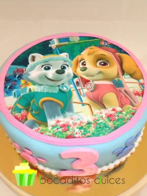 Tarta cubierta de fondant azul con pequeñas huellas de cachorro de fondant alrededor de la tarta, con una foto de los protagnistas de la serie en papel de azúcar.