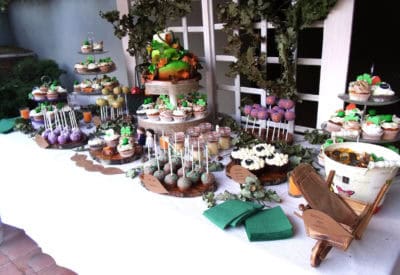 Mesa dulce compuesta por cupcakes de diferentes sabores, cupcakes imitando la forma de una oveja, cake pops cubiertos de candy mels morado decorados con bolitas de caramelo naranjas, cakepops chocolate decorados con chocolate fundido verde, tarritos de cristal con bizcocho,y tarta de tres pisos decorada con fondant dondo forma a hojas de forma otoñal.