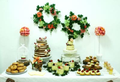 Mesa dulce compuesta por nubes de gominola, nini vasos de bizcocho y buttercream, pastelitos , galletas de mantequilla, donuts, tarta desnuda de tres pisos decorada con furtas del bosque y tarta semidesnuda, decorada con flores de fondant