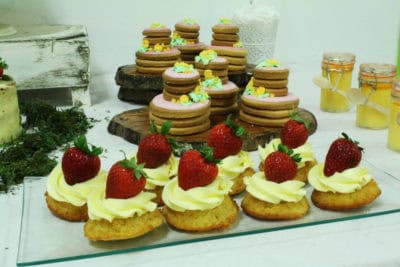 Mesa dulce compuesta por nubes de gominola, nini vasos de bizcocho y buttercream, pastelitos , galletas de mantequilla, donuts, tarta desnuda de tres pisos decorada con furtas del bosque y tarta semidesnuda, decorada con flores de fondant