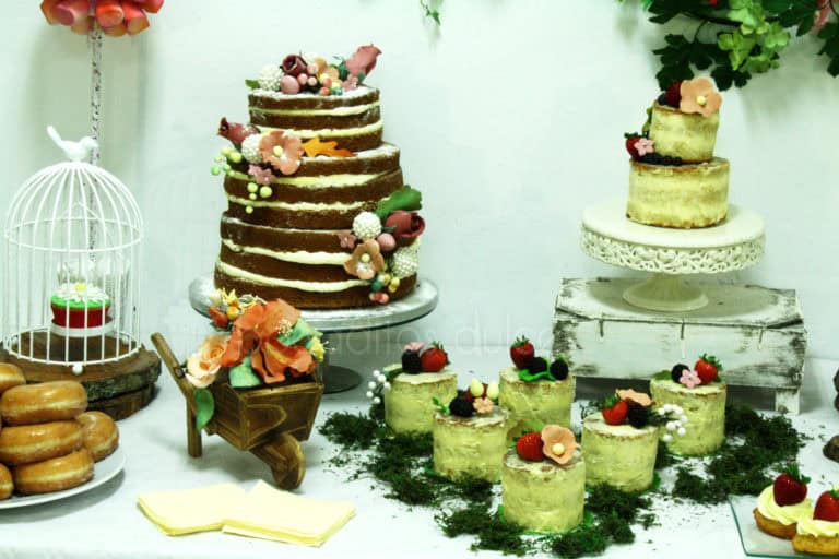 Mesa dulce compuesta por nubes de gominola, nini vasos de bizcocho y buttercream, pastelitos , galletas de mantequilla, donuts, tarta desnuda de tres pisos decorada con furtas del bosque y tarta semidesnuda, decorada con flores de fondant