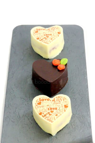 Pequeños pastelitos de frutas, cubiertos con chocolate blanco y con leche, decorados con letras de papel de azúacar, y pequeñas flores de fondant