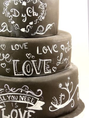 Tarta de tres pisos cubierta de fondant negro, y decorada con dibujos y tetras con tinta blanca comestible.
