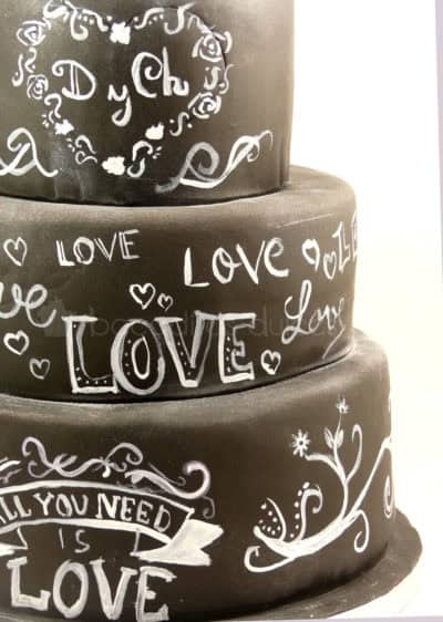 Tarta de tres pisos cubierta de fondant negro, y decorada con dibujos y tetras con tinta blanca comestible.