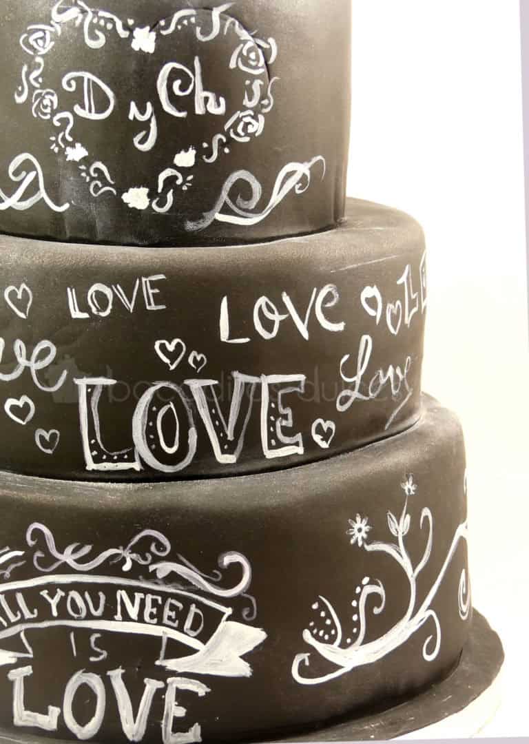 Tarta de tres pisos cubierta de fondant negro, y decorada con dibujos y tetras con tinta blanca comestible.