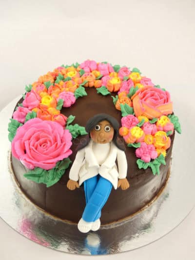 Tarta cubierta de ganache de chocolate, decorada con flores de buttercream de colores y muñeca personalizada en fondant