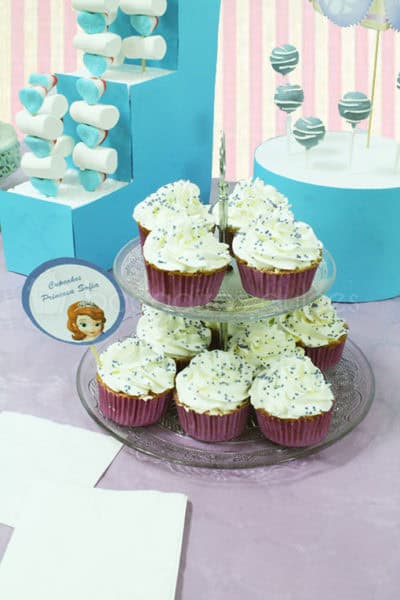 Mesa dulce compuesta por cake pops cubiertos de candy mels azul y chocolate blanco fundido, cajitas personalizadas con palomitas, cupcakes de vainilla, galletas de mantequilla con forma de coroza cubiertas de fondant , brochetas de chuches, y bolas de chicle.