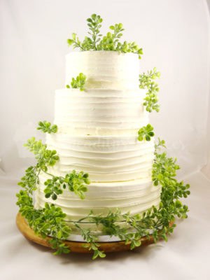 Tarta de cuatro pisos, cubierta de buttercream de color blanco, decorada con hojas .