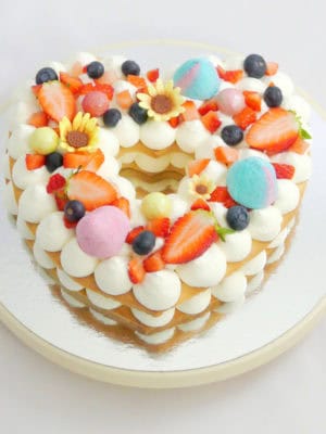 tarta con forma de corazón, base de galleta, crema de queso y decoración de frutas, chuches y chocolates.